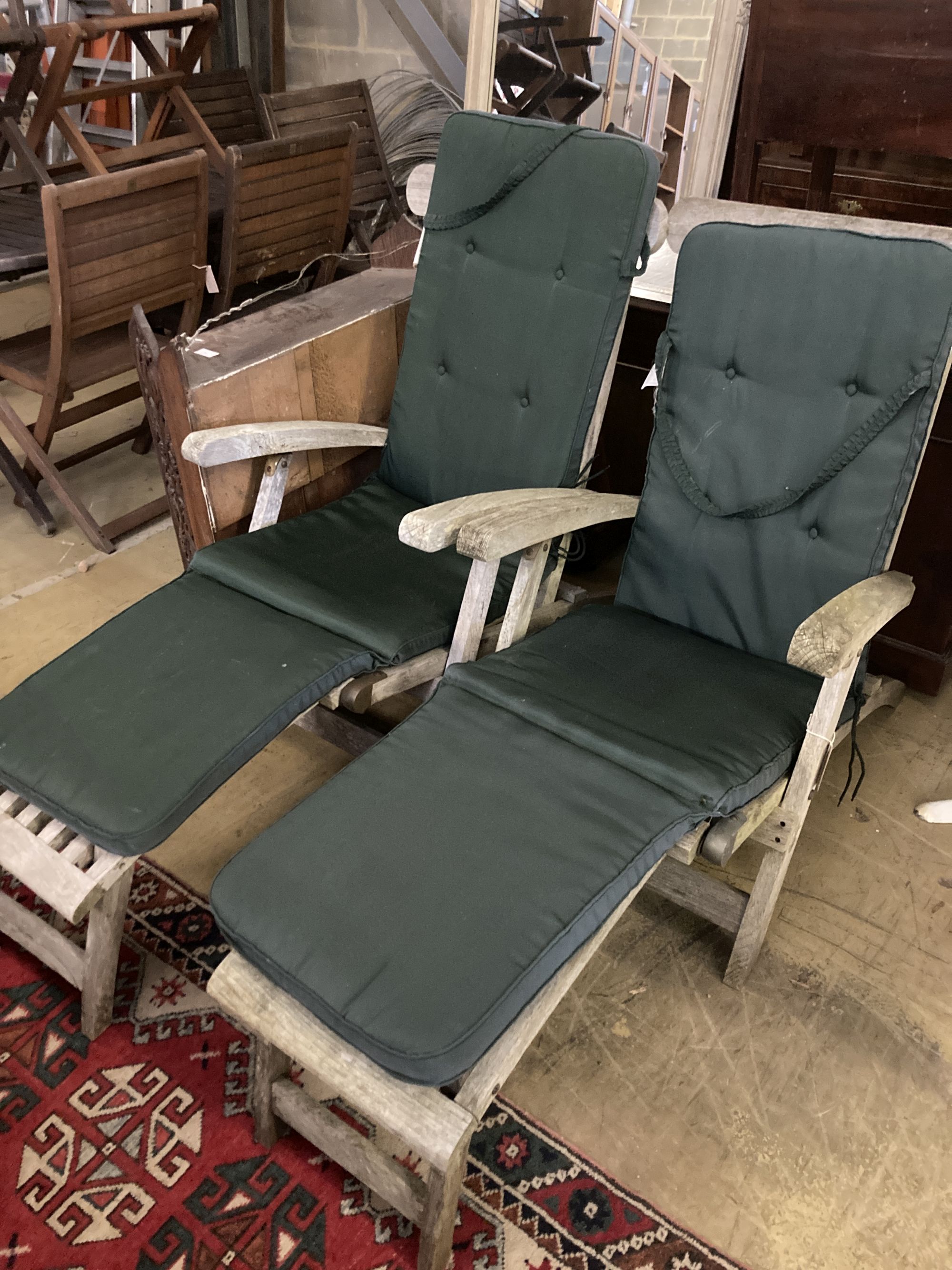 A pair of weathered teak steamer garden chairs with cushions